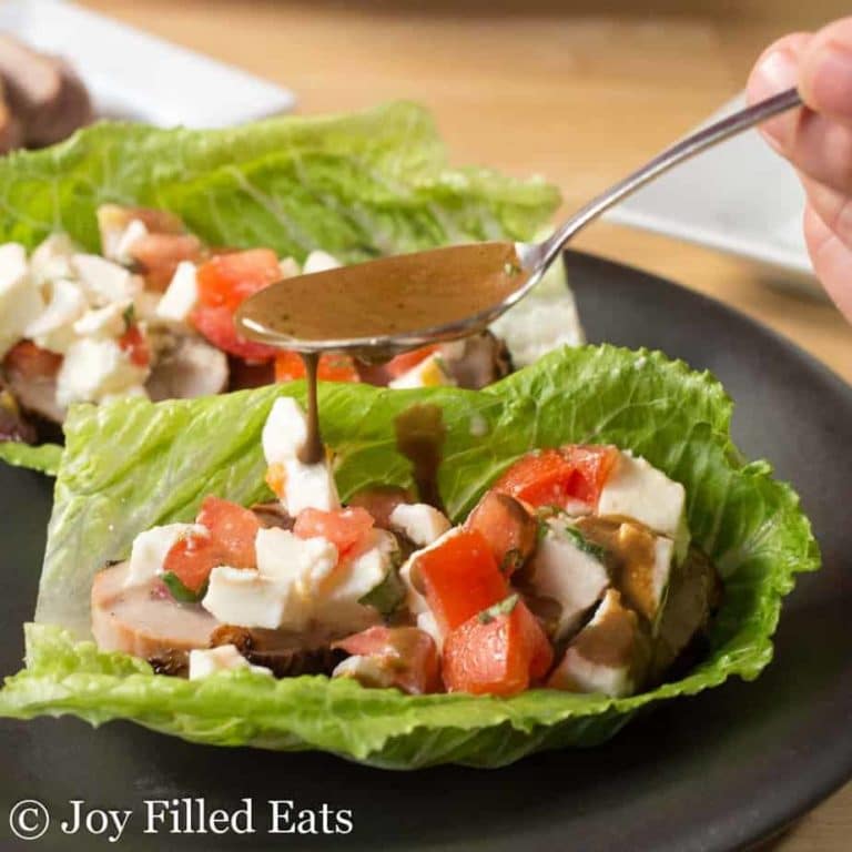 keto father's day recipes Grilled pork tenderloin caprese salad lettuce wraps on a plate being drizzled with balsamic dressing on a wooden table