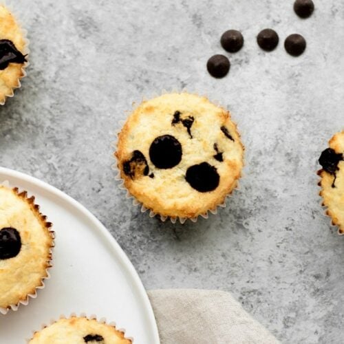 low carb chocolate chip banana bread muffins surrounded by chocolate chips atop a marble kitchen counter