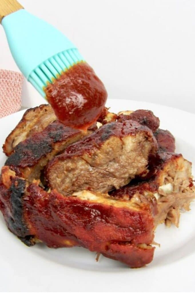 keto father's day recipes Instant Pot Baby Back Ribs being wiped with bbq sauce on a plate atop a white marble table counter