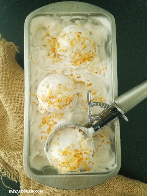 keto summer recipes - a tub of keto coconut ice cream being scooped by an ice cream scooper atop a wooden table
