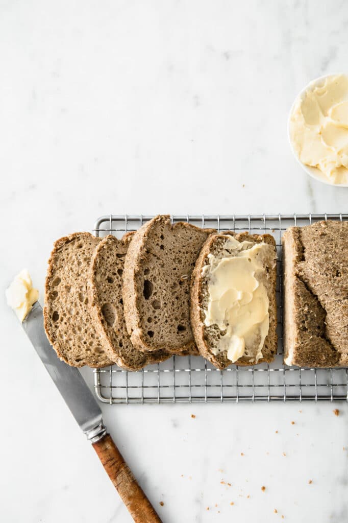 slices of nut-free keto bread with butter resting on a wire rack atop a marble kitchen counter
