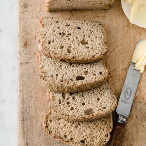 half a loaf and 4 slices of nut-free keto bread resting on a wooden board with a bread knife dipped in butter