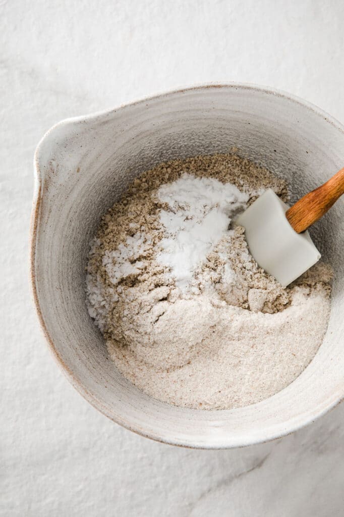 dry ingredients mixed with egg yolk mixture using a rubber spatula in a mixing bowl atop a marble kitchen counter