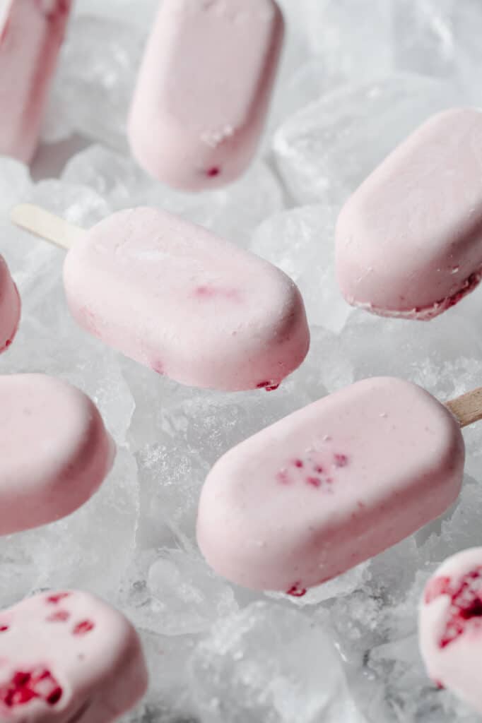 close-up side angle shot of berry cream popsicles laying flat atop ice cubes