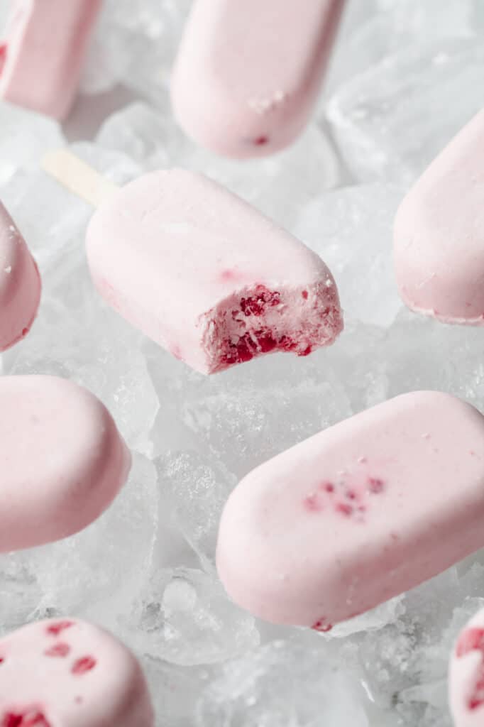 berry cream popsicles laying flat atop ice cubes with bite taken out of one popsicle