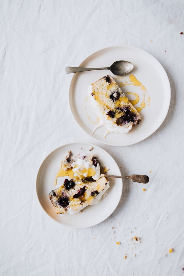 overhead view of 2 plates with a spoon and a slice of keto lemon blueberry bread each atop a marble kitchen counter