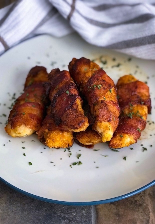 six bacon-wrapped parmesan-crusted chicken on a plate atop a wooden table