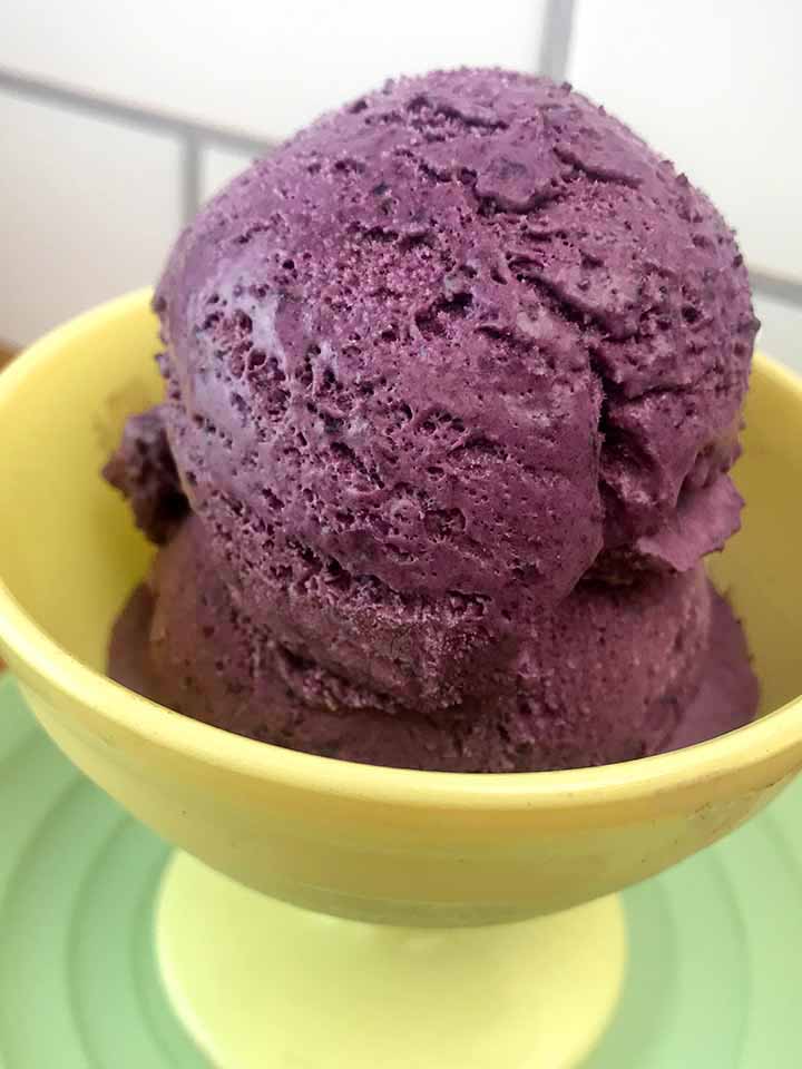 a big scoop of keto blueberry ice cream in a yellow ice cream bowl atop a table