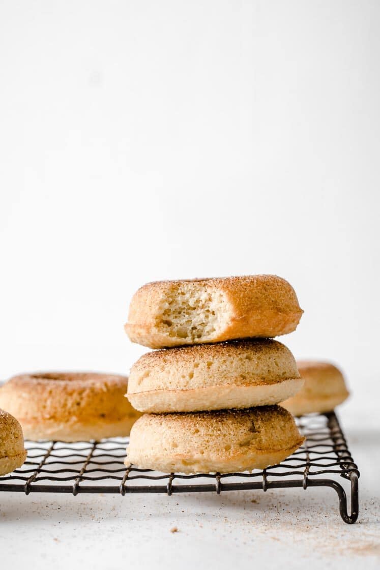 3 nut-free keto donuts stacked on top of each other resting on a wire rack atop amarble kitchen counter