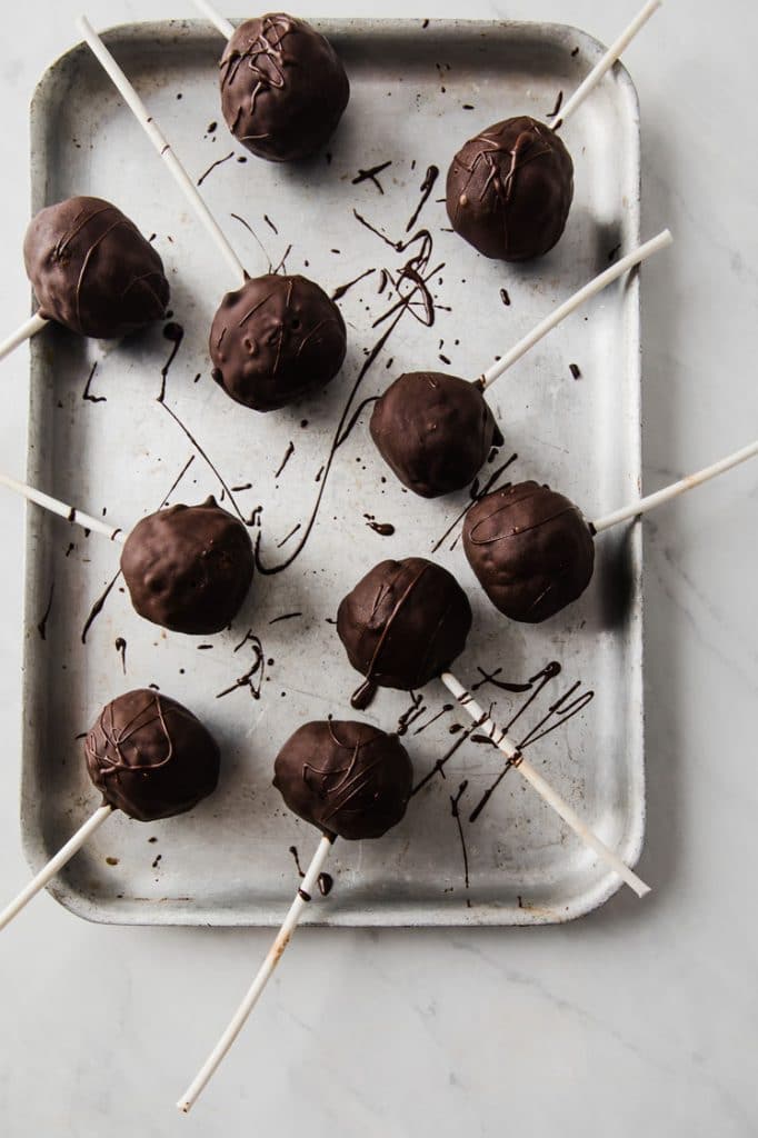 overhead image of chocolate covered pumpkin pie cake pops on a parchment paper-lined baking sheet atop a marble kitchen counter