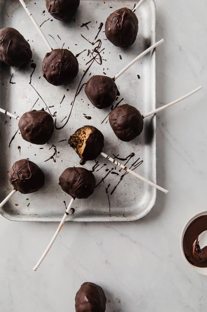 pumpkin pie cake pops on a parchment paper-lined baking sheet atop a marble kitchen counter