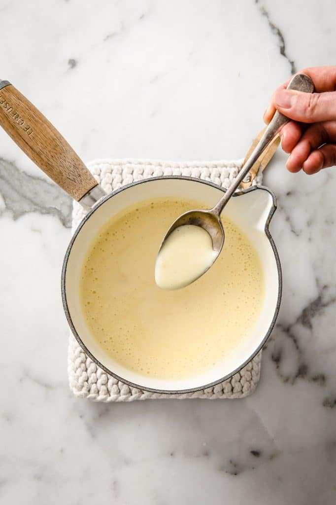 sweetened condensed milk being cooked in a sauce pan resting atop a marble kitchen counter