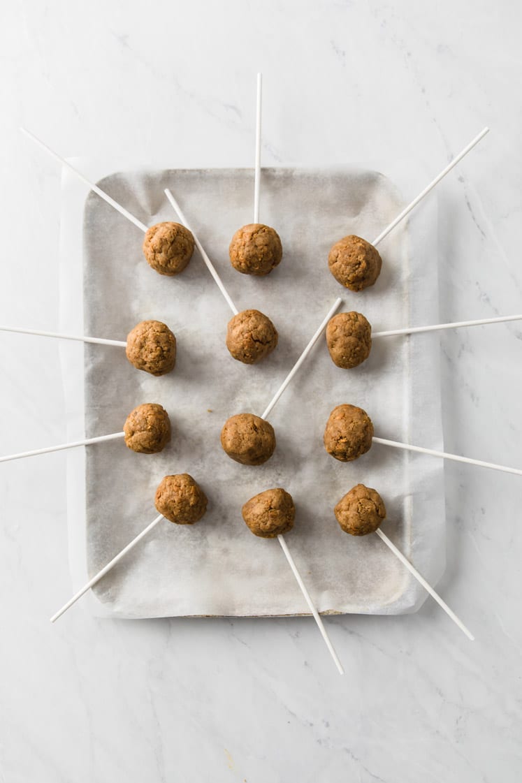 pumpkin pie cake balls skewered with lollipop sticks on a parchment paper-lined baking sheet