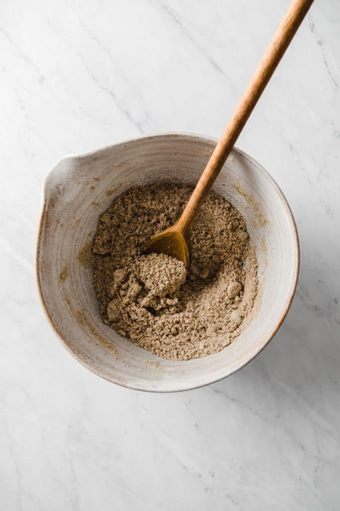 dry ingredients mixed by a wooden spatula in a mixing bowl atop a marble kitchen counter