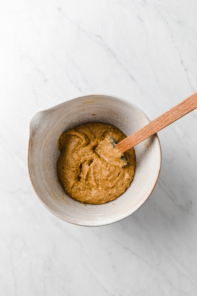 dry ingredients mixed with egg yolk mixture being mixed with a rubber spatula in a mixing bowl atop a marble kitchen table