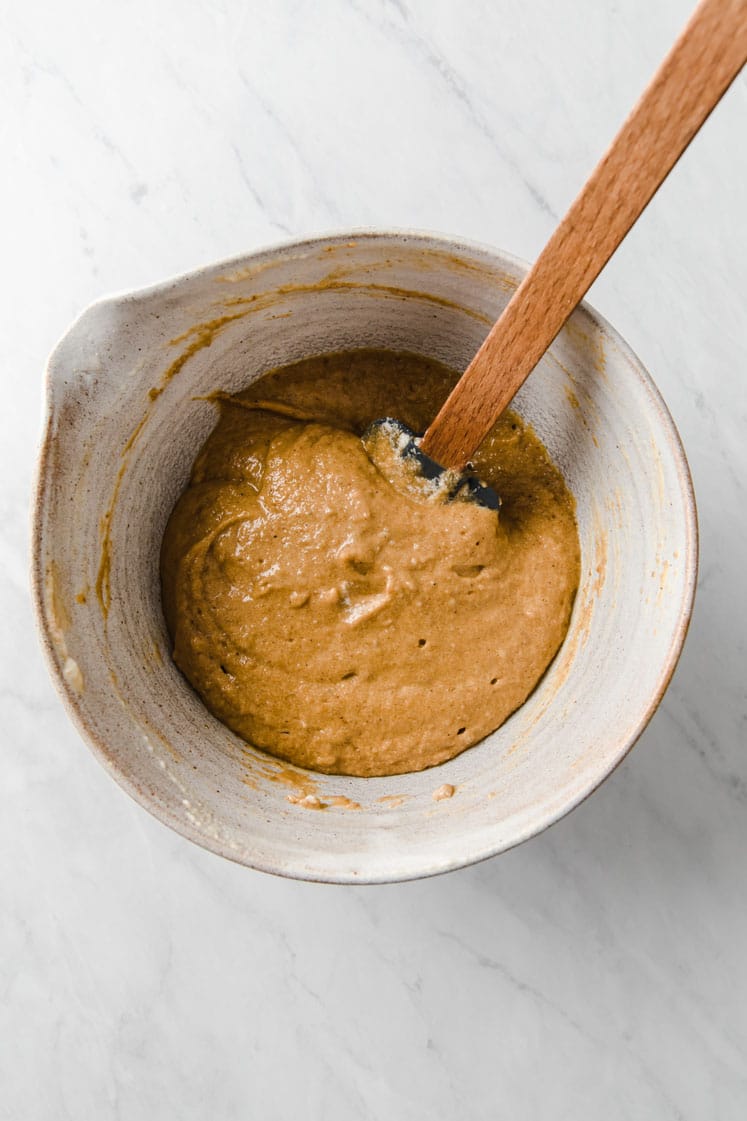 pumpkin puree and melted butter being mixed with batter in a mixing bowl atop a marble kitchen table