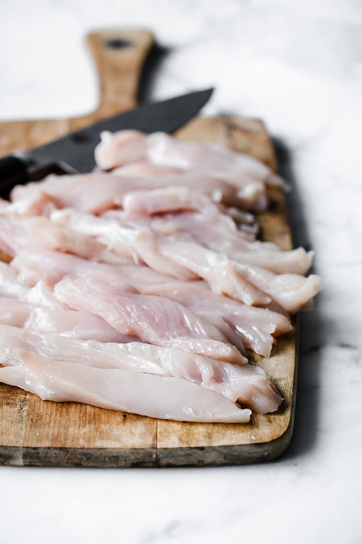 chicken breast cut into strips on a chopping board