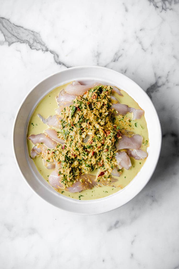 overhead image of chicken strips soaked in coconut marinade atop a marble kitchen counter