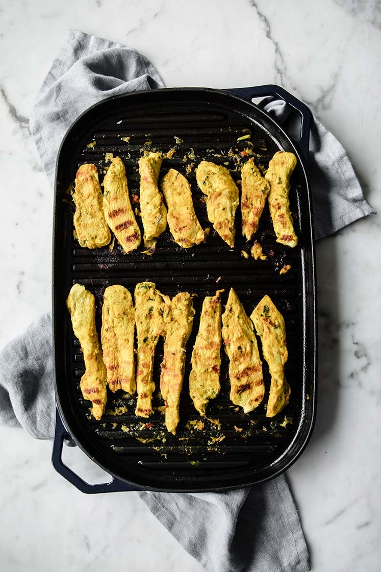 chicken strips being cooked on an even layered pan atop a marble kitchen table.