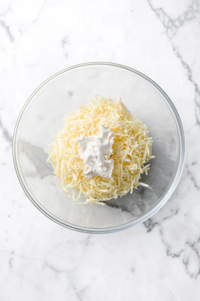 shredded mozzarella cheese in a mixing bowl atop a marble kitchen counter