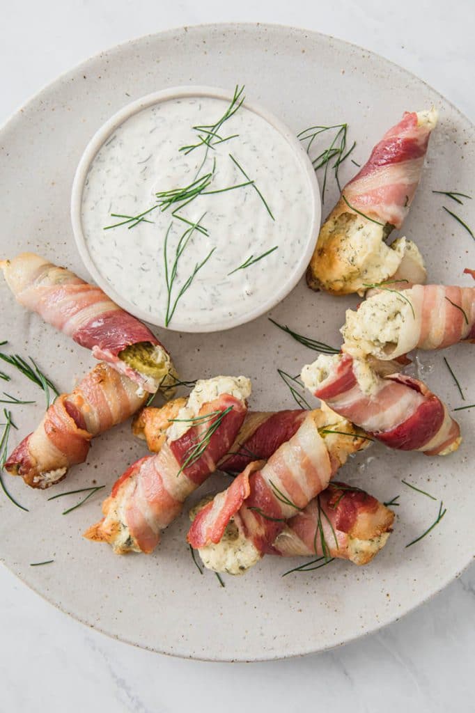keto pickle poppers with a bowl of ranch on a plate atop a marble kitchen counter