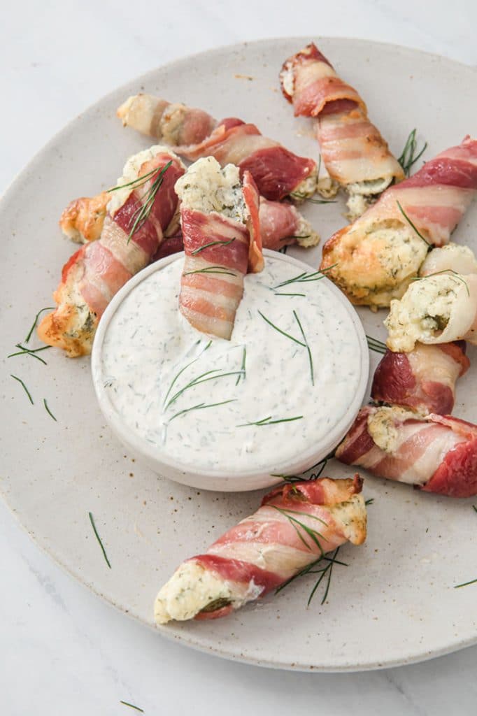 keto pickle poppers dipped in a bowl of ranch on a plate atop a marble kitchen counter