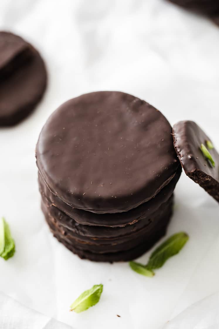 angled shot of a stack of keto thin mints atop with some mint leaves on the side atop a marble kitchen counter