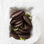 overhead image of a baking pan lined with baking paper filled with keto thin mints sprinkled with mint leaves atop a marble kitchen counter