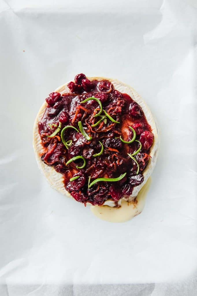 close-up image of keto baked brie on a parchment paper-lined baking sheet topped with sugar-free cranberry sauce atop a marble kitchen counter