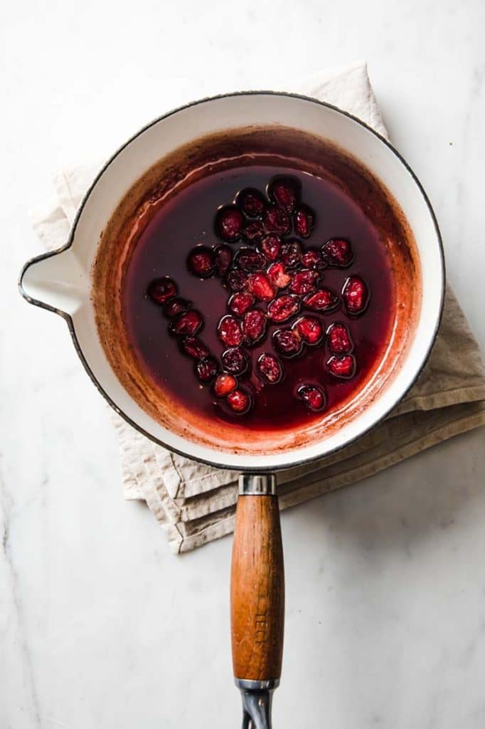 overhead image of cranberry sauce, cooked until cranberries are soft in a saucepan atop a marble kitchen counter