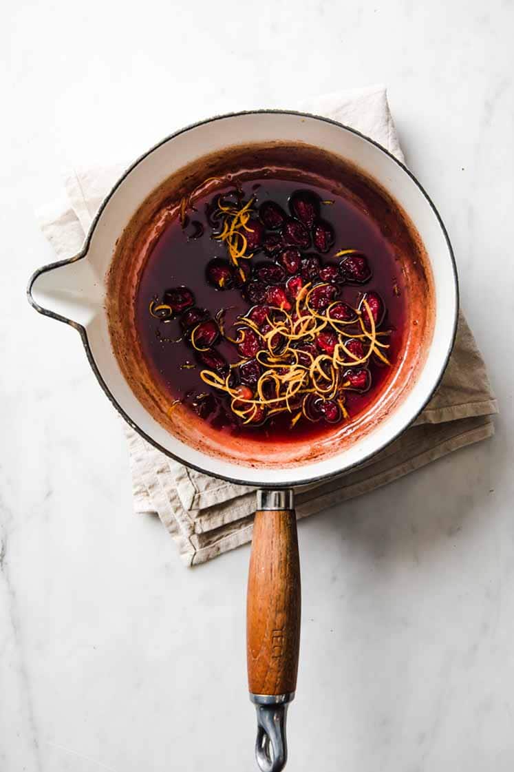 a saucepan of cranberry sauce topped with orange zest atop a marble kitchen table