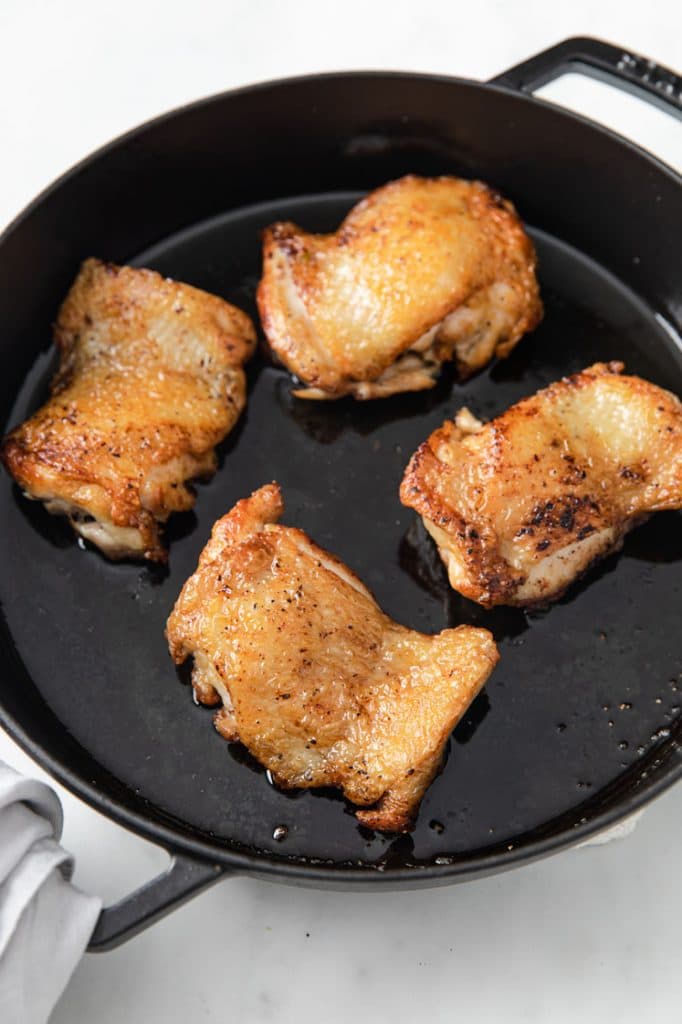 4 chicken thighs cooked until skin has browned on a cast iron skillet atop a marble kitchen table