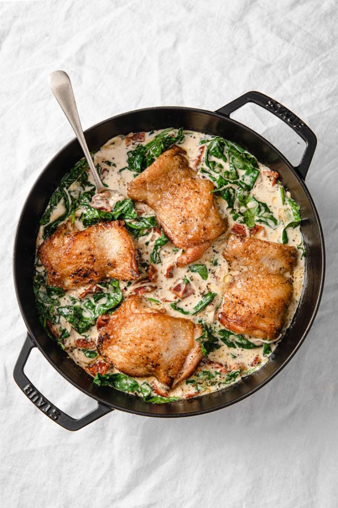 overhead image of 4 creamy tuscan chicken thighs on a nonstick pan atop a marble kitchen counter