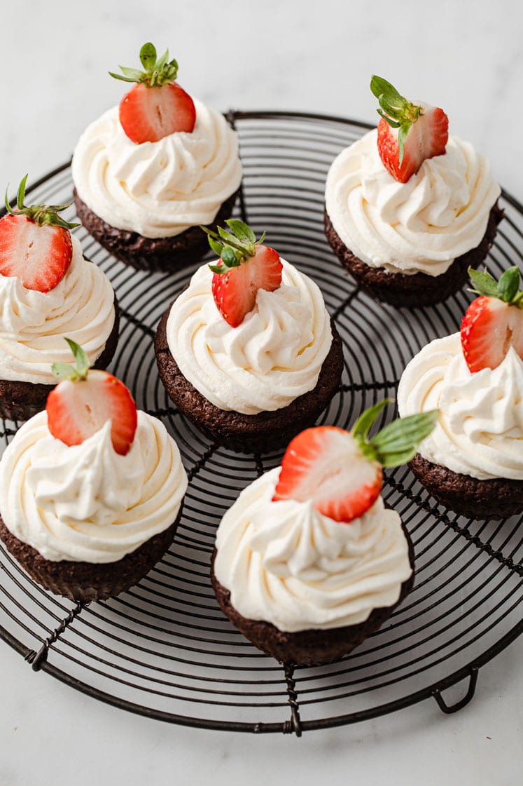 featured recipe image of 7 chocolate strawberry cupcakes topped with sliced strawberries resting on a wire-rack atop a marble kitchen counter
