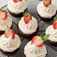 close-up featured recipe image of 7 chocolate strawberry cupcakes topped with sliced strawberries resting on a wire-rack atop a marble kitchen counter