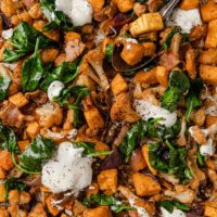 overhead close-up image of a tray full of roasted butternut squash and cauliflower with bacont, topped with sour cream