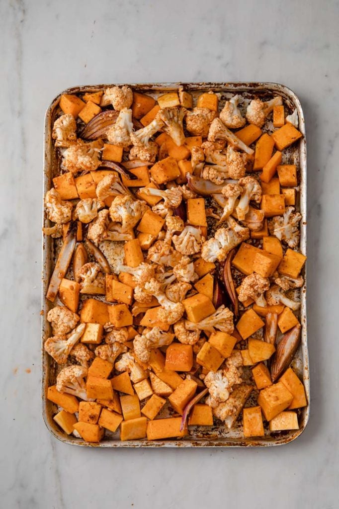 overhead image of butternut squash, cauliflower, and onion on a baking tray atop a marble kitchen counter