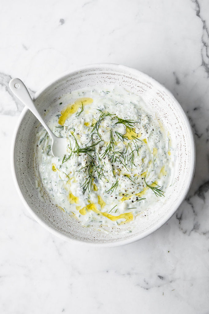 Garnished tzatziki in a bowl with a spoon.