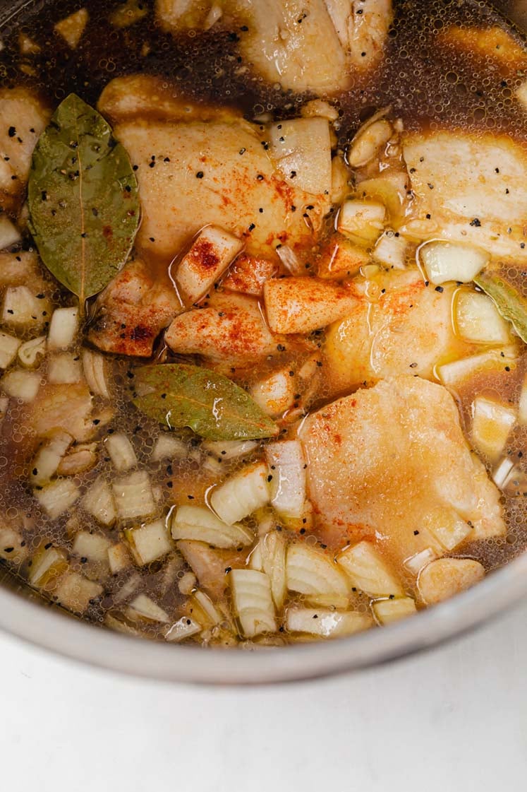 chicken thighs still in pot, with added chicken stock, coconut aminos, onion, garlic, vinegar, bay leaves, monk fruit sweetener, and paprika.