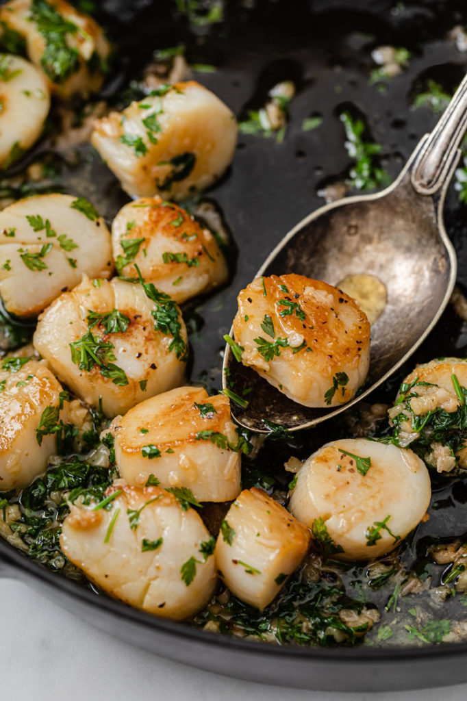 image of a scallop scooped by a spoon from a pan of lemon garlic scallops