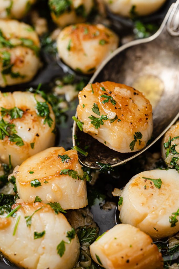 close-up image of a scallop scooped by a spoon from a pan of lemon garlic scallops