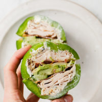 a hand holding green bell pepper sandwich atop cutting board and marble countertop