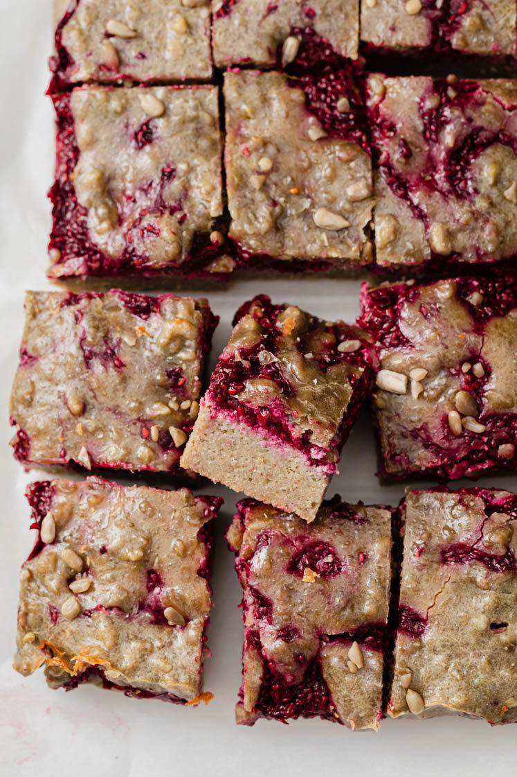 close-up image of raspberry crumble bars on a baking sheet lined by parchment paper atop a marble kitchen counter
