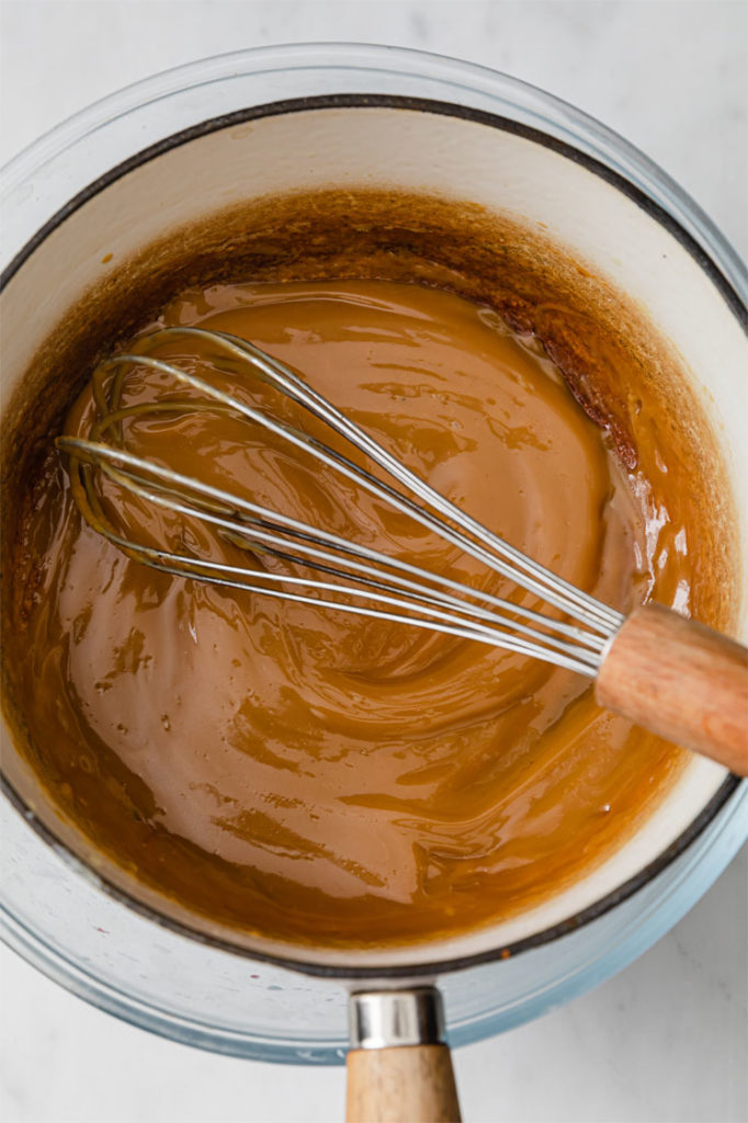 caramel being stirred in a saucepan atop a marble kitchen table.