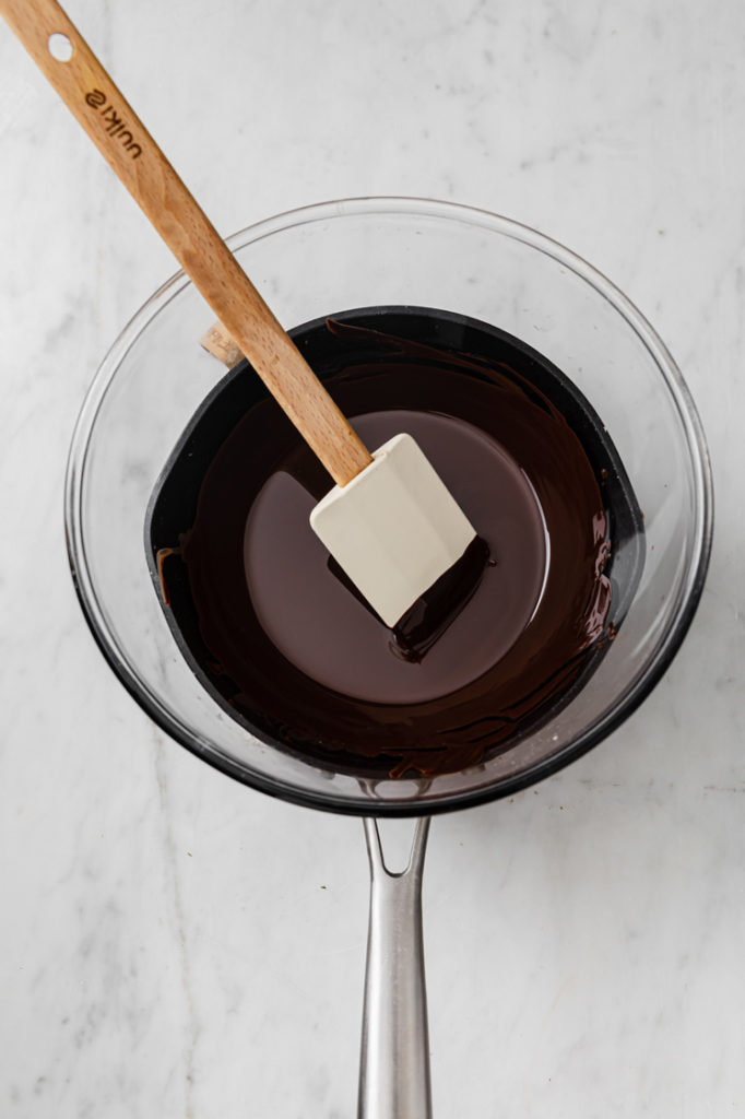 melted chocolate being stirred in a saucepan atop a marble kitchen table.