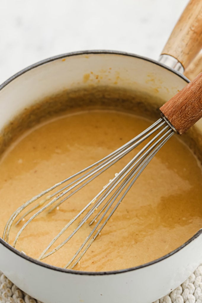 a mixture of melted butter and heavy cream mixture being stirred by a whisk in a saucepan.
