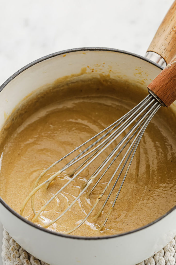 a mixture of melted butter, heavy cream mixture, and Sunbutter being stirred by a whisk in a saucepan.