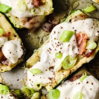 Loaded Zucchini Boats garnished with a dollop of sour cream and green onions atop a baking sheet.