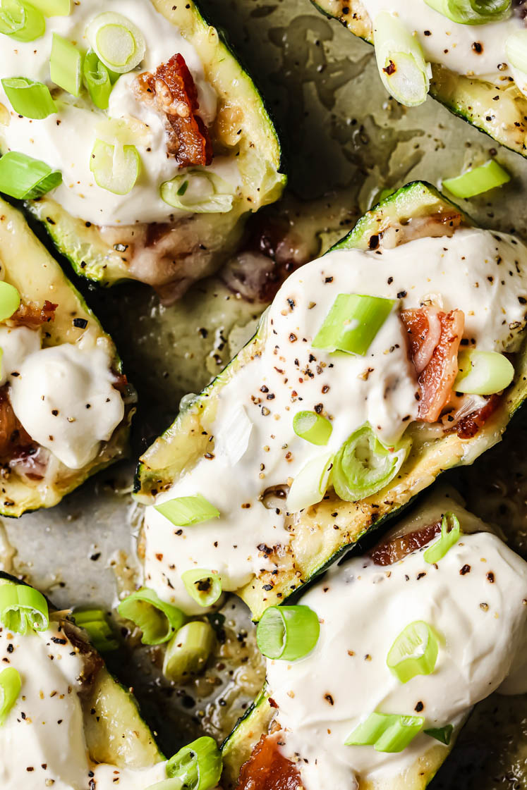 Loaded Zucchini Boats garnished with a dollop of sour cream and green onions atop a baking sheet.