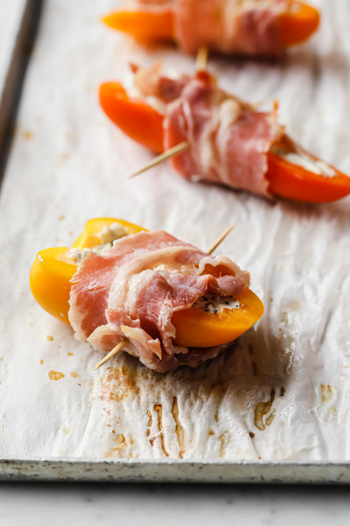 peppers wrapped in bacon secured by a toothpick on a parchment paper lined baking tray.